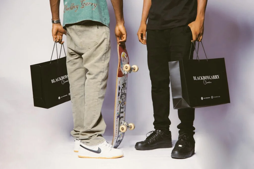 Two individuals holding shopping bags and skateboard in stylish casual attire.